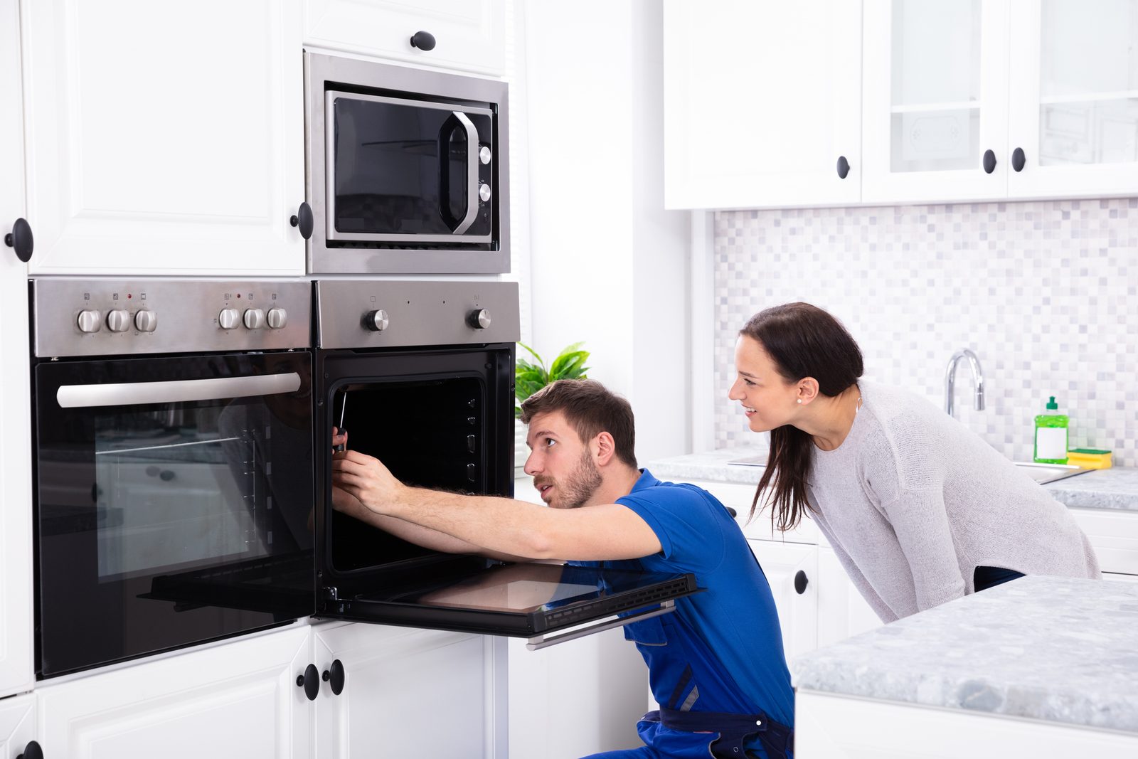 Technicien réparant un four au domicile d'une cliente